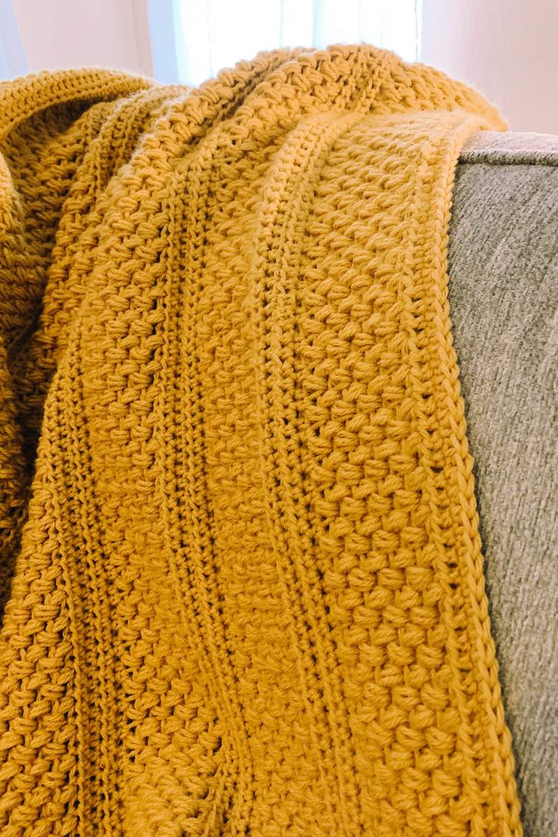 yellow crochet blanket draped over a gray couch